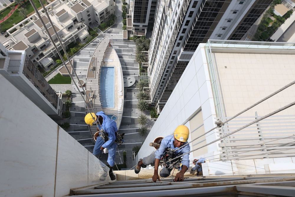 Two construction workers using safety ropes on the exterior of a high-rise building.